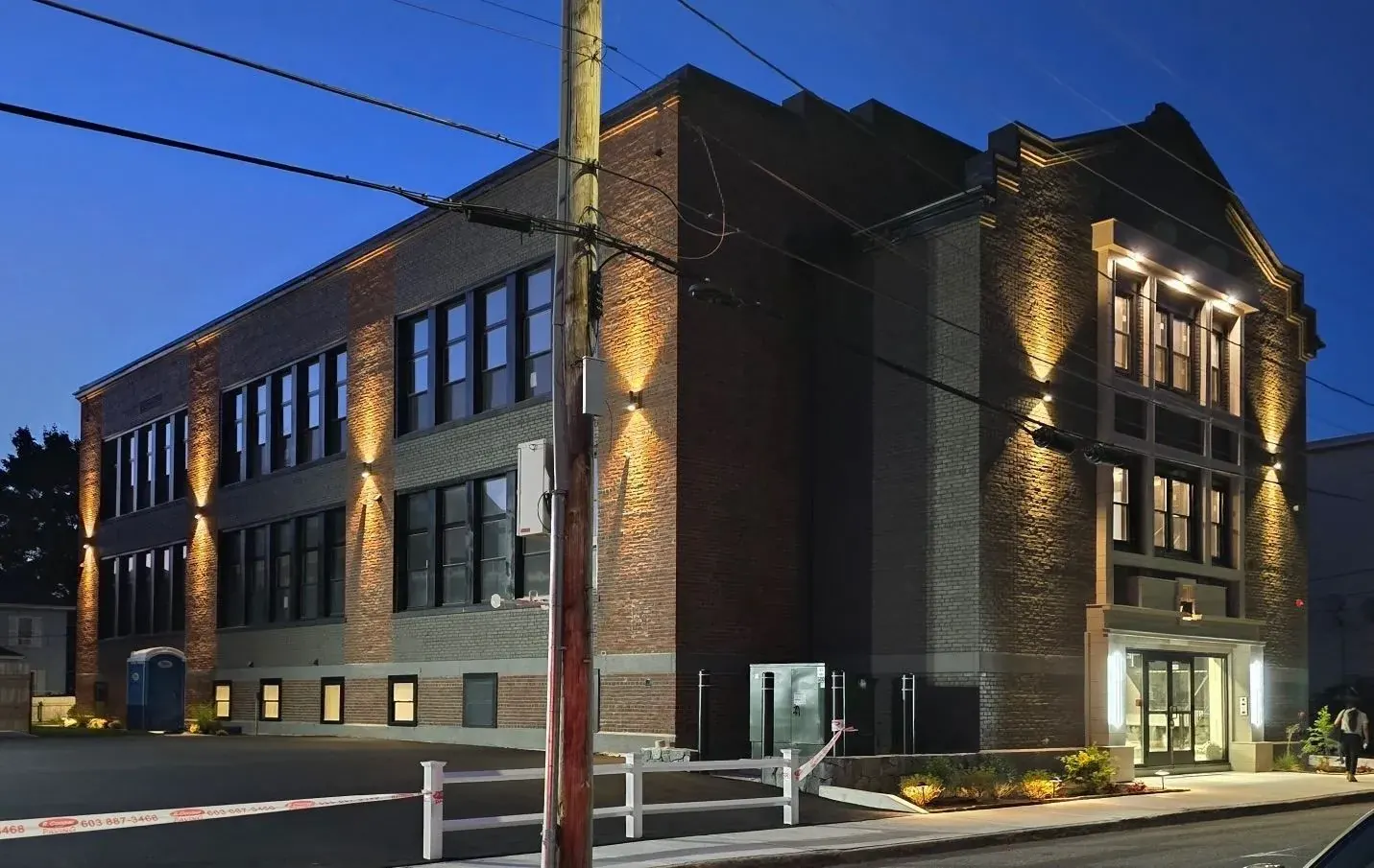 Three-story brick building washed with exterior wall lights at dusk