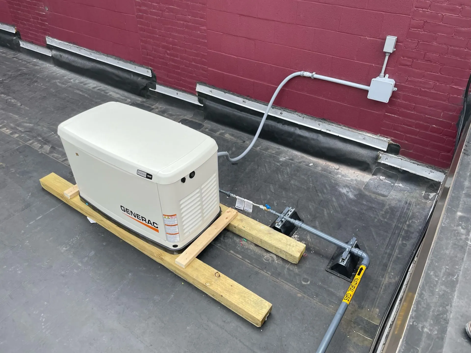 Standby generator set on a flat roof with conduit run to a junction box on the brick wall
