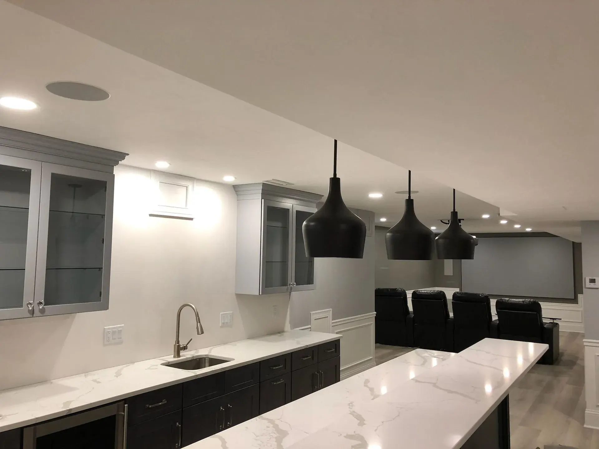 Basement wet bar with black pendants beside a media room