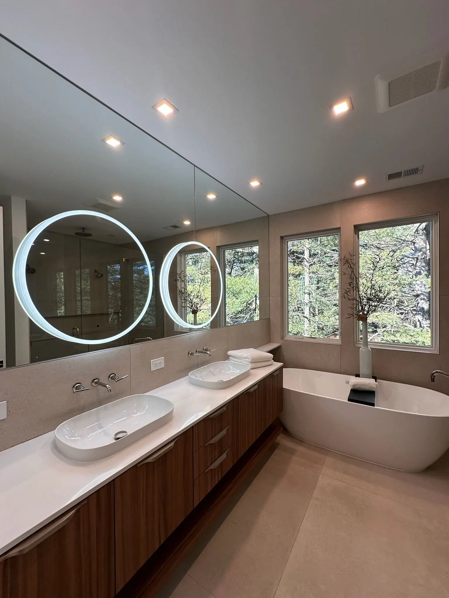 Primary bathroom with round backlit mirrors, recessed lights and a freestanding tub