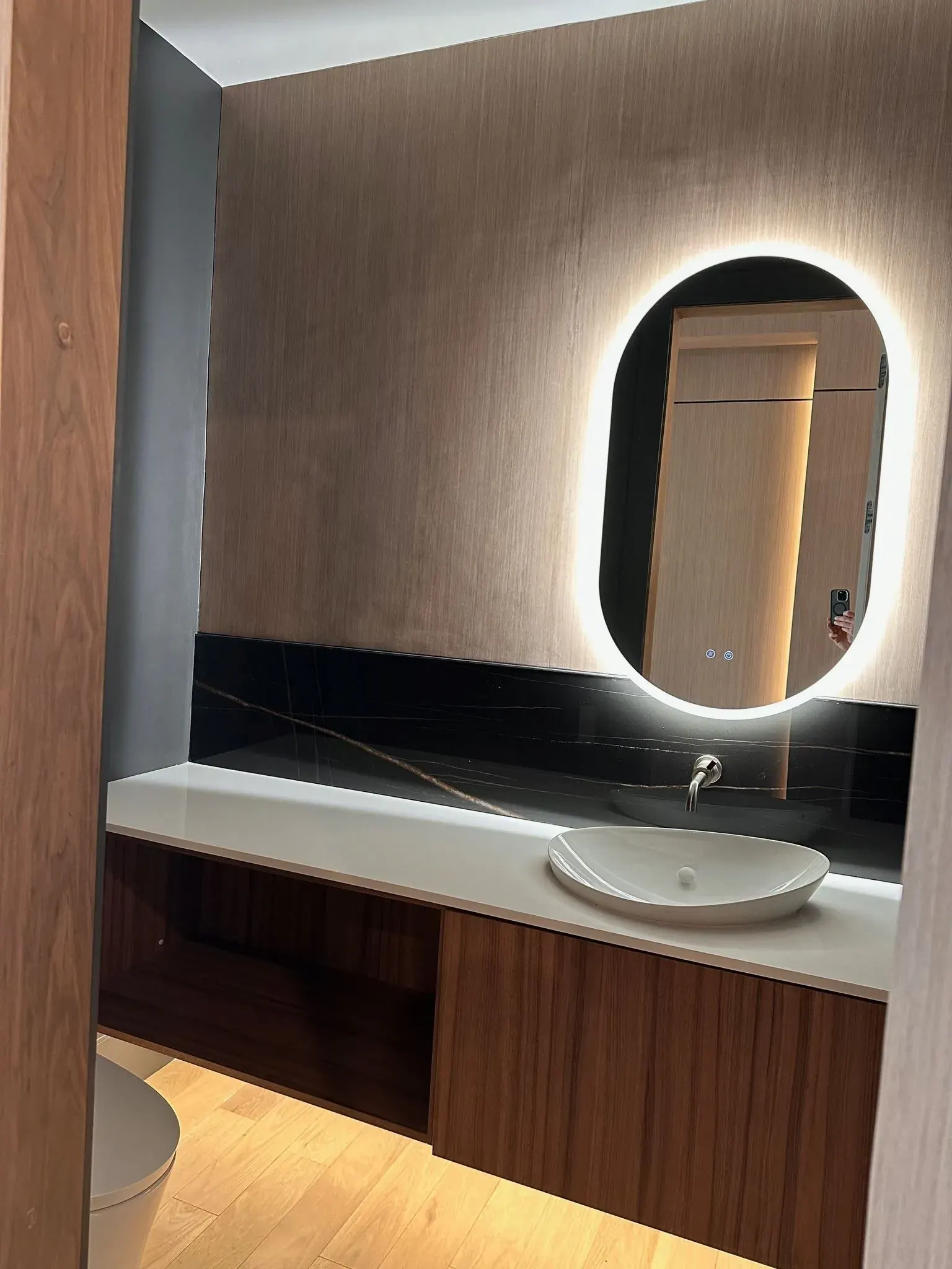 Powder room with a backlit oval mirror and under-vanity light