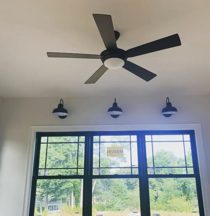 Dark five-blade ceiling fan above black barn-style wall sconces