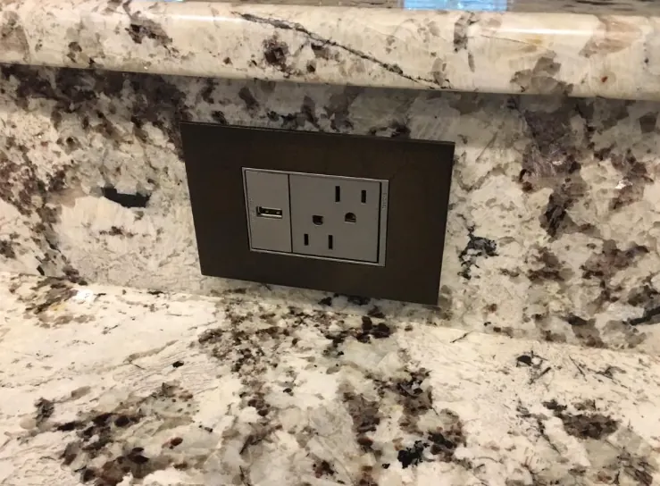 USB combination outlet with a bronze plate set into a granite backsplash