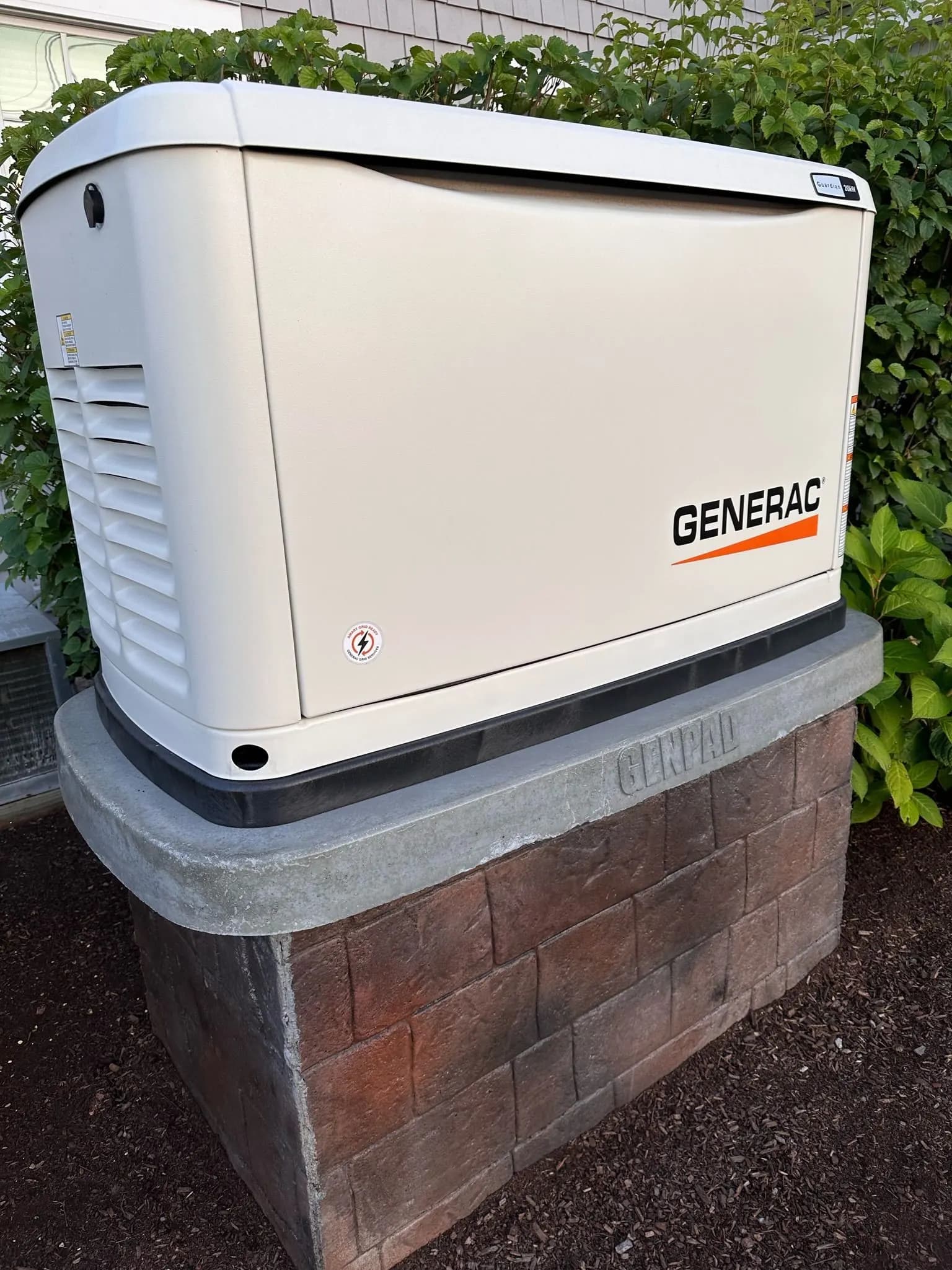 Generac home standby generator mounted on a stone pedestal beside a house