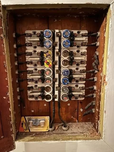 Old screw-in fuse box in a wood-backed wall cavity before replacement